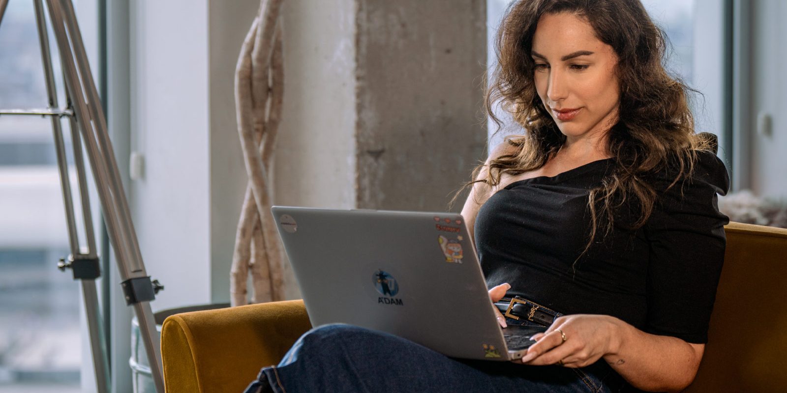 Een vrouw die op de bank zit met haar laptop op schoot bij de coworking space van A'DAM&Co.work in de A'DAM Toren Amsterdam